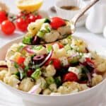 A spoon holds a serving of Greek Cauliflower Salad above the bowl.