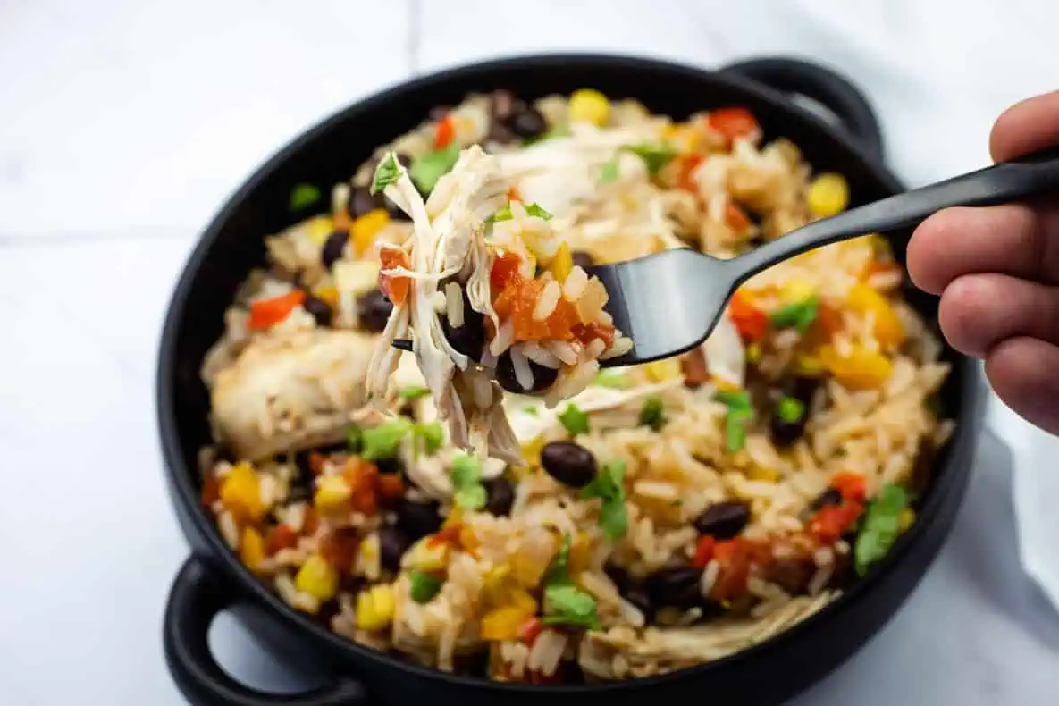 A close-up of a fork holding a bite of Slow Cooker Santa Fe Chicken over a bowl with the same mixed dish.