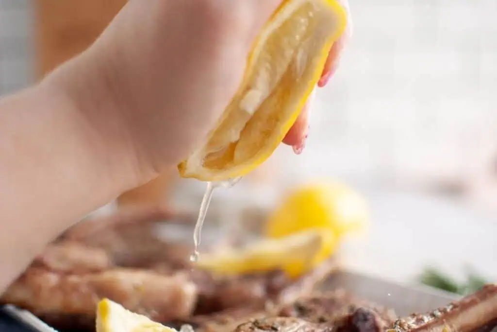 A hand squeezing a lemon wedge over cooked meat, with lemon juice dripping onto the food below.