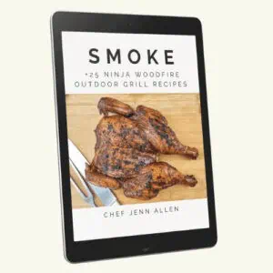 An e-book cover on a tablet displays "Smoke: 25+ Ninja Woodfire Outdoor Grill Recipes" with a grilled spatchcock chicken and utensils, authored by Chef Jenn Allen.