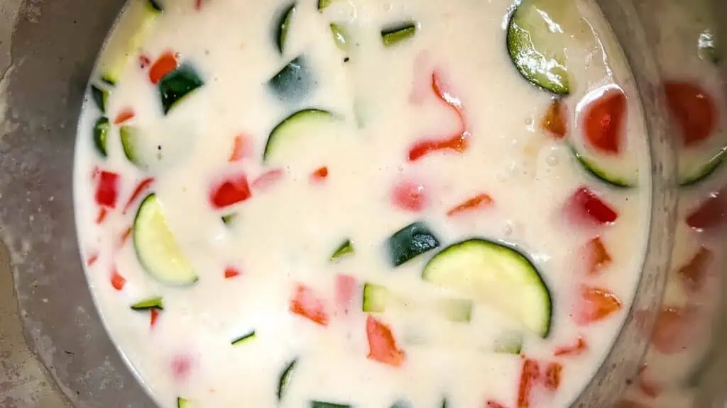 Bowl of thick, creamy batter mixed with chopped vegetables including zucchini and red bell pepper.