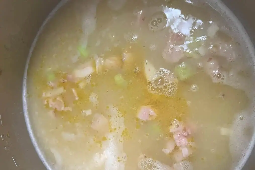 A pot of broth with chunks of meat, and small pieces of vegetables.