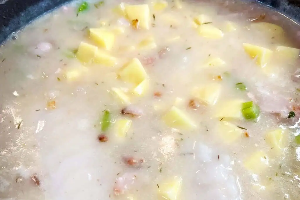 A close-up of a creamy soup with diced potatoes, celery, and bits of bacon in a light broth.