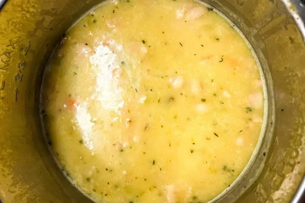 A close-up view of creamy soup with visible chunks of vegetables and herbs in a metal pot.