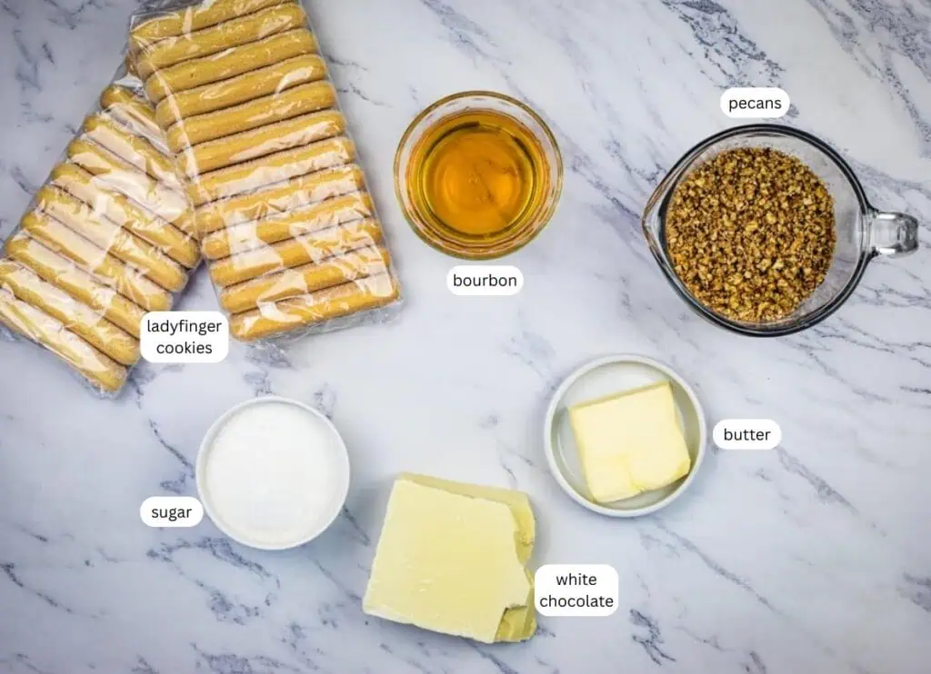 Ingredients on a marble surface: packaged ladyfinger cookies, bourbon in a glass bowl, chopped pecans, sugar, white chocolate, and butter, each labeled.