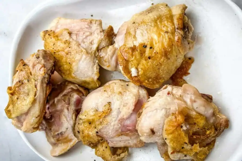 Six pieces of cooked chicken thighs with browned skin arranged on a white oval plate.