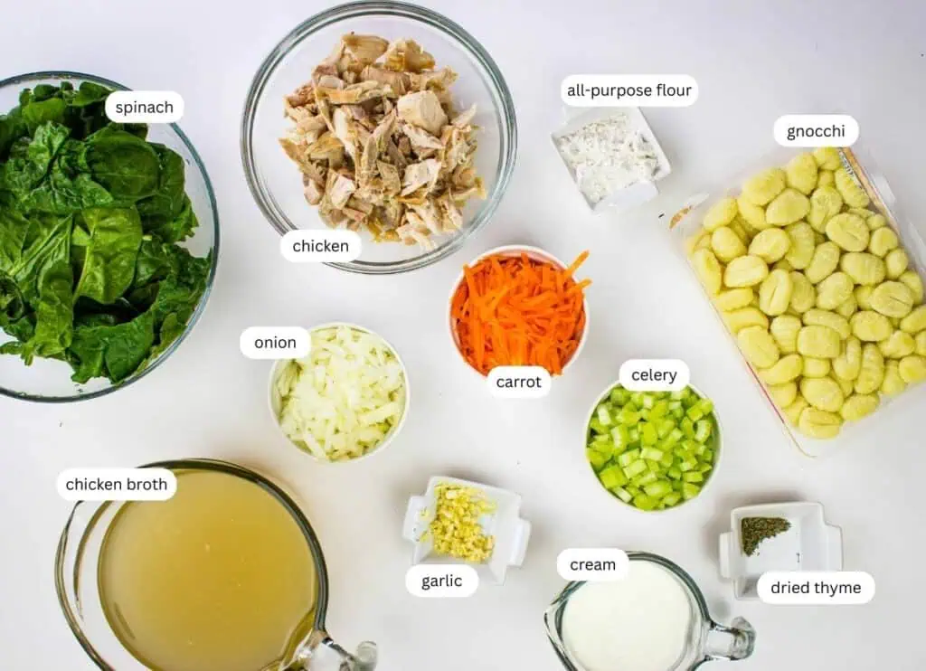Top-down view of labeled ingredients for creamy chicken gnocchi soup, including spinach, chicken, gnocchi, onion, carrot, celery, garlic, chicken broth, cream, all-purpose flour, and dried thyme.