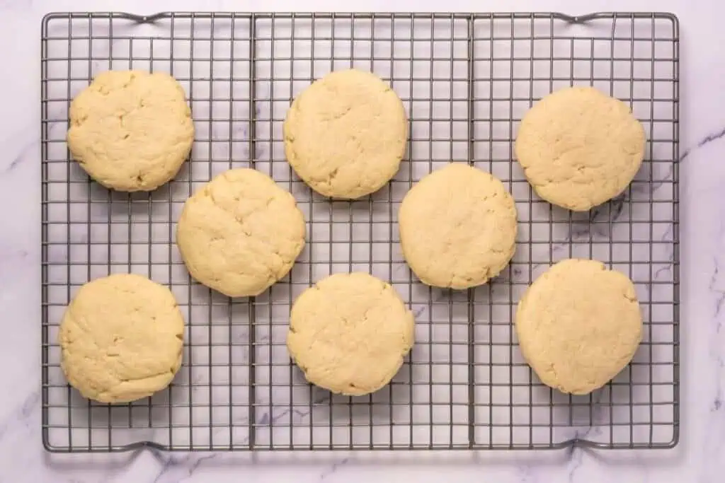 Eight plain round cookies cooling on a metal wire rack over a white marble surface.