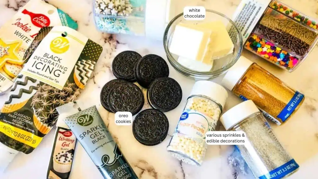 A variety of baking supplies including Oreo cookies, white chocolate, black decorating icing, sparkle gel, and various sprinkles and edible decorations arranged on a white surface.