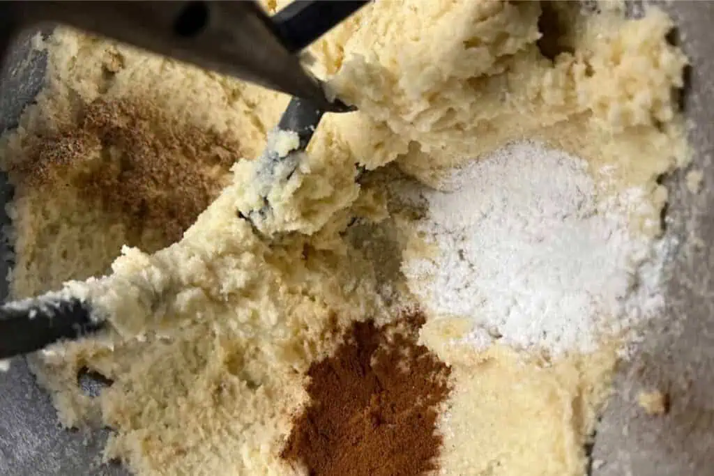 Close-up of cookie dough in a mixing bowl with visible flour and spices before being fully mixed.