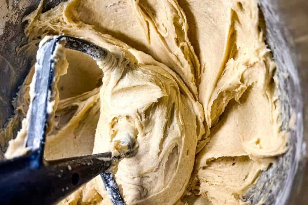 Close-up of a metal mixing paddle in a bowl of thick, creamy cookie dough.