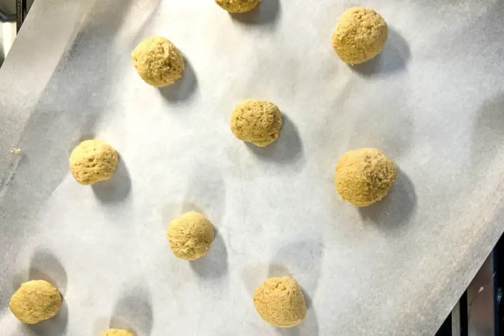 Ten unbaked cookie dough balls are arranged on a parchment-lined baking sheet, ready to be baked.