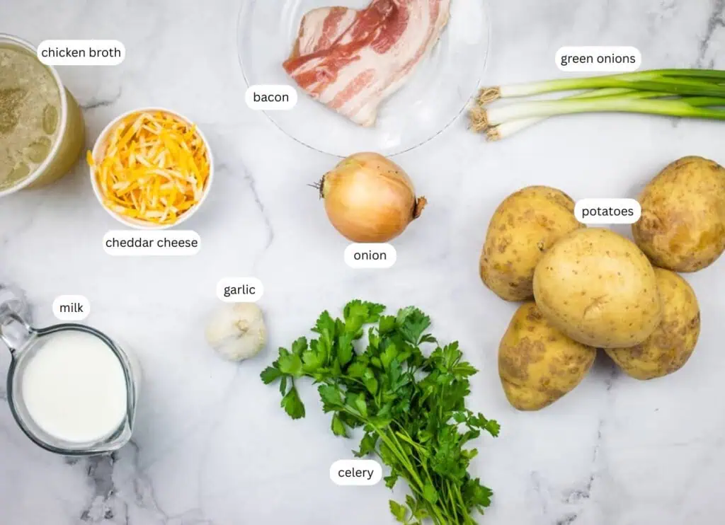 Ingredients for a potato soup recipe, including chicken broth, bacon, green onions, cheddar cheese, onion, potatoes, milk, garlic, celery, and parsley, arranged on a marble surface.