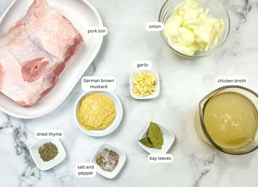 Raw pork loin, chopped onion, minced garlic, German brown mustard, chicken broth, dried thyme, bay leaves, salt, and pepper are arranged in bowls on a marble surface.