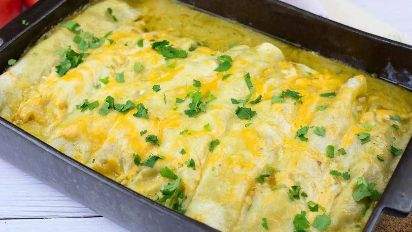 A baking dish filled with enchiladas topped with melted cheese and garnished with chopped cilantro.