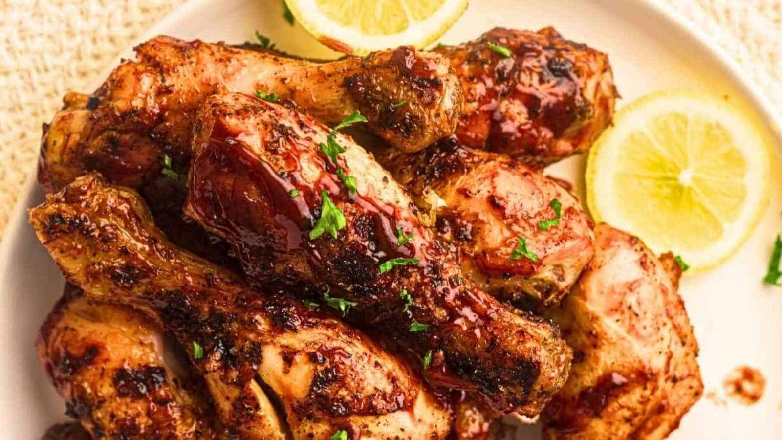 A plate of grilled chicken drumsticks garnished with chopped herbs, served with lemon slices.