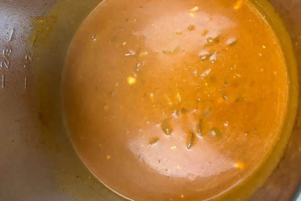A close-up view of brown gravy with small bits of herbs and spices in a pot, with measurement markings visible on the side.