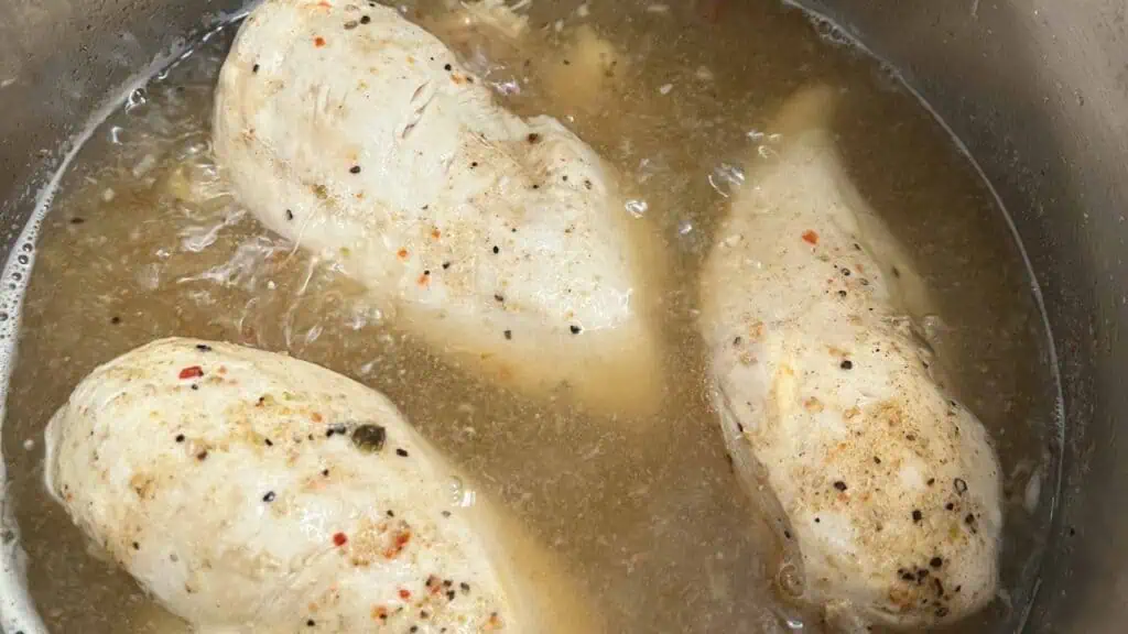 Three seasoned chicken breasts simmering in a pot of broth.