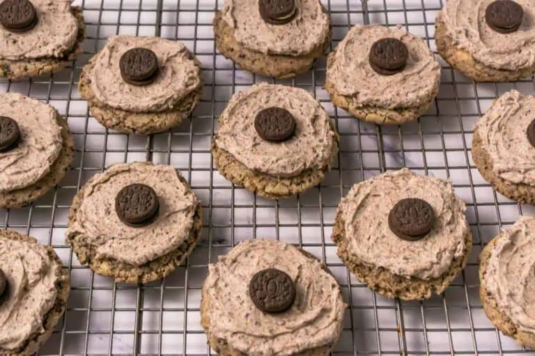 Chocolate chip cookies topped with swirled chocolate frosting and a mini chocolate sandwich cookie, arranged on a cooling rack.