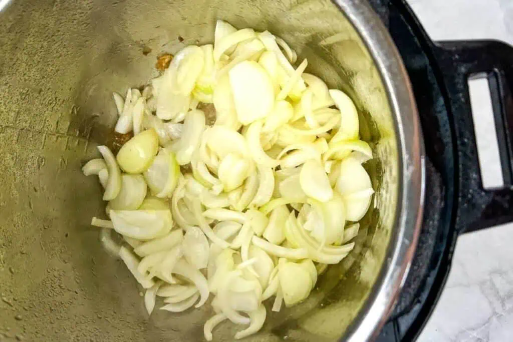 Sliced onions and garlic cloves cooking in a stainless steel pot on a stovetop or electric cooker.