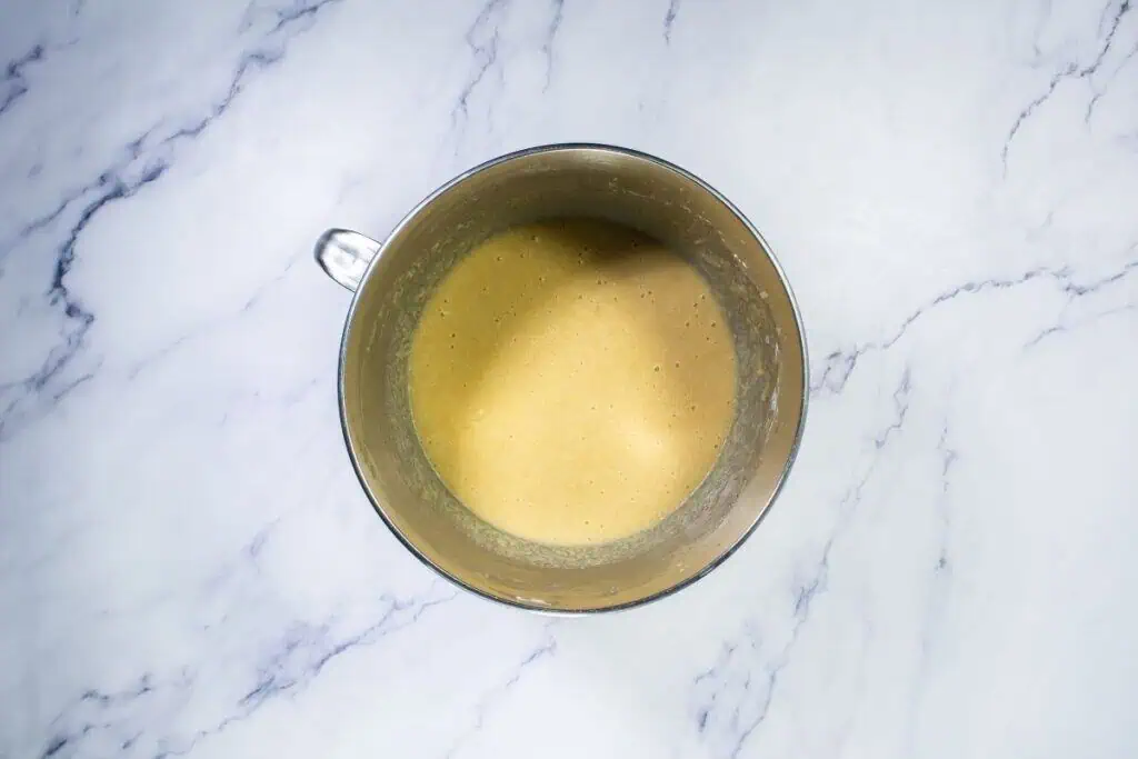 A metal mixing bowl filled with a smooth, light brown batter sits on a white marble surface.