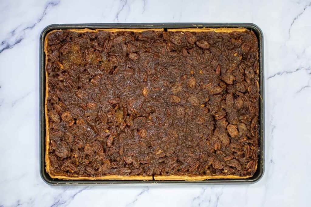 A rectangular sheet pan filled with baked pecan bars on a marble surface.