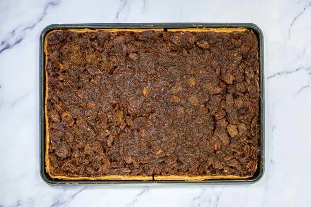 A rectangular sheet pan filled with baked pecan bars on a marble surface.