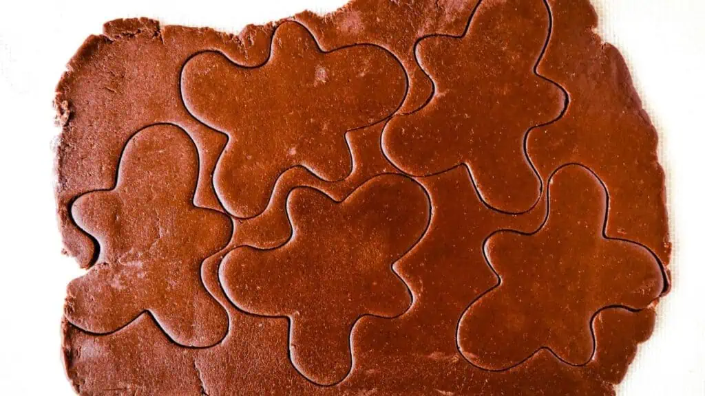 Rolled out chocolate cookie dough with several gingerbread-shaped figures cut out, ready to be separated and baked.