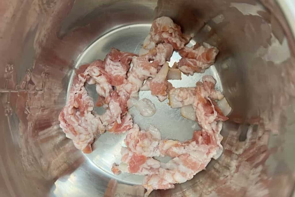 Raw chopped bacon pieces in a stainless steel pot.