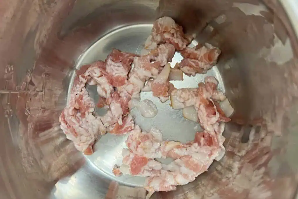 Raw chopped bacon pieces in a stainless steel pot.