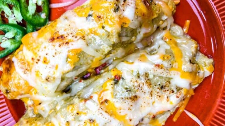 Two cheesy enchiladas topped with melted cheese are served on a red plate, with sliced jalapeños on the side.