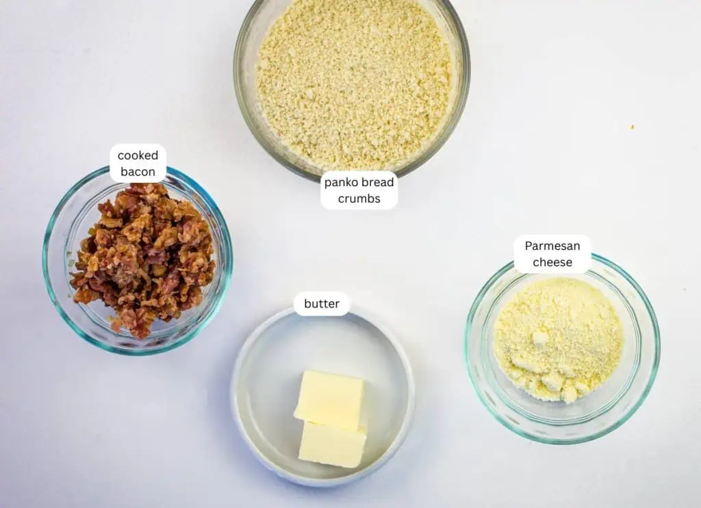 Four bowls containing panko bread crumbs, cooked bacon, butter, and Parmesan cheese, each labeled, arranged on a white surface.