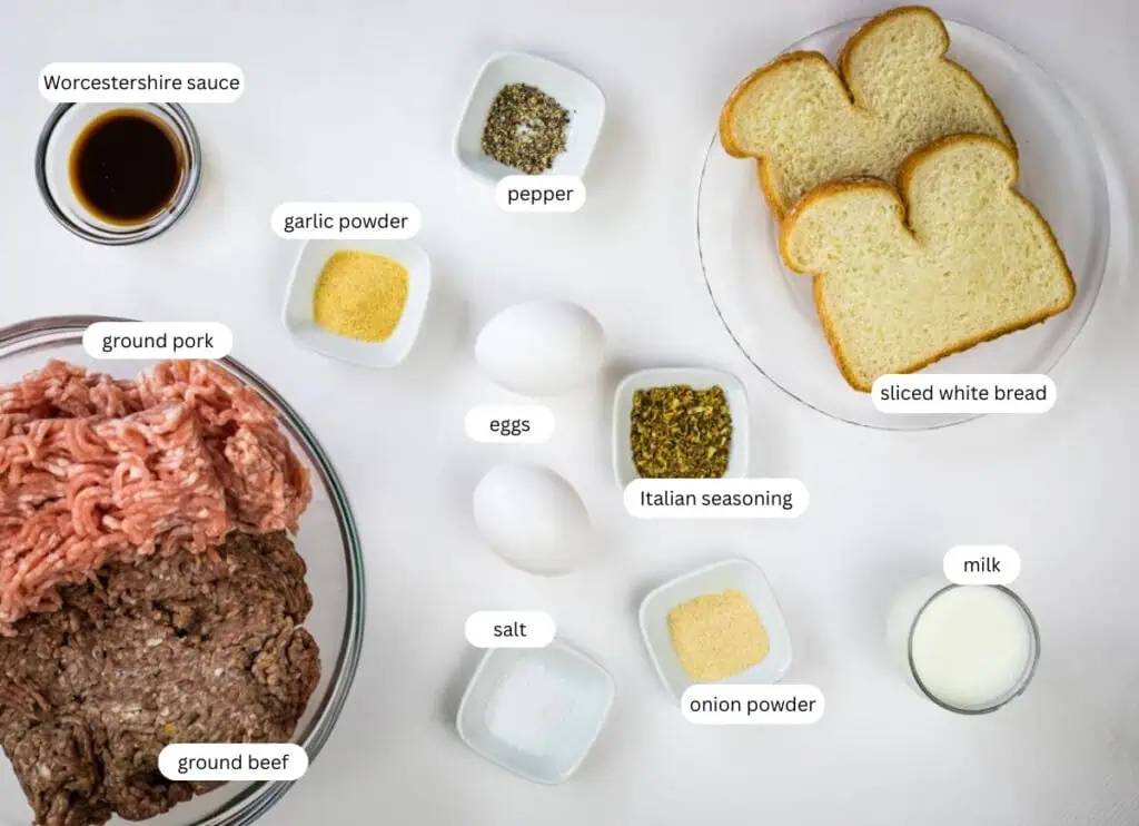 Ingredients for smoked meatballs, including ground beef, ground pork, eggs, milk, sliced white bread, Worcestershire sauce, seasonings, salt, pepper, garlic powder, and onion powder, are arranged on a table.