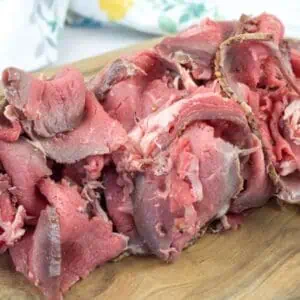 Slices of rare roast beef arranged on a wooden cutting board.
