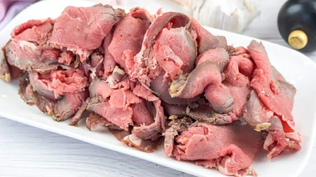 A white rectangular plate filled with slices of rare roast beef, showing pink centers and browned edges.