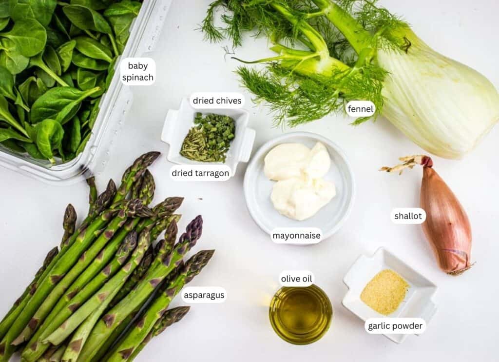 Fresh baby spinach, fennel, asparagus, and shallot are arranged on a white surface alongside small bowls of mayonnaise, olive oil, garlic powder, dried tarragon, and dried chives.