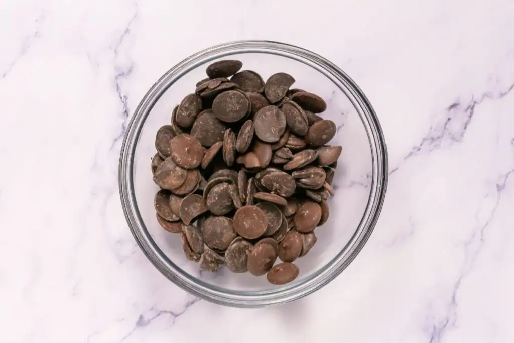 A glass bowl filled with chocolate wafers sits on a white marble surface.