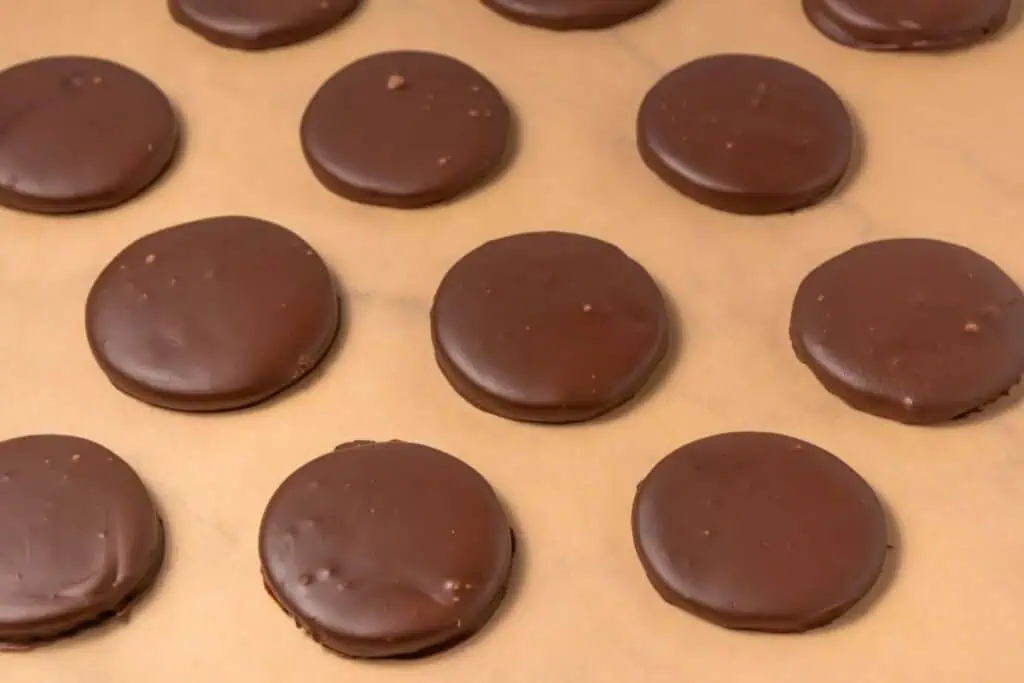 Rows of round, chocolate-covered cookies are arranged on a sheet of parchment paper.