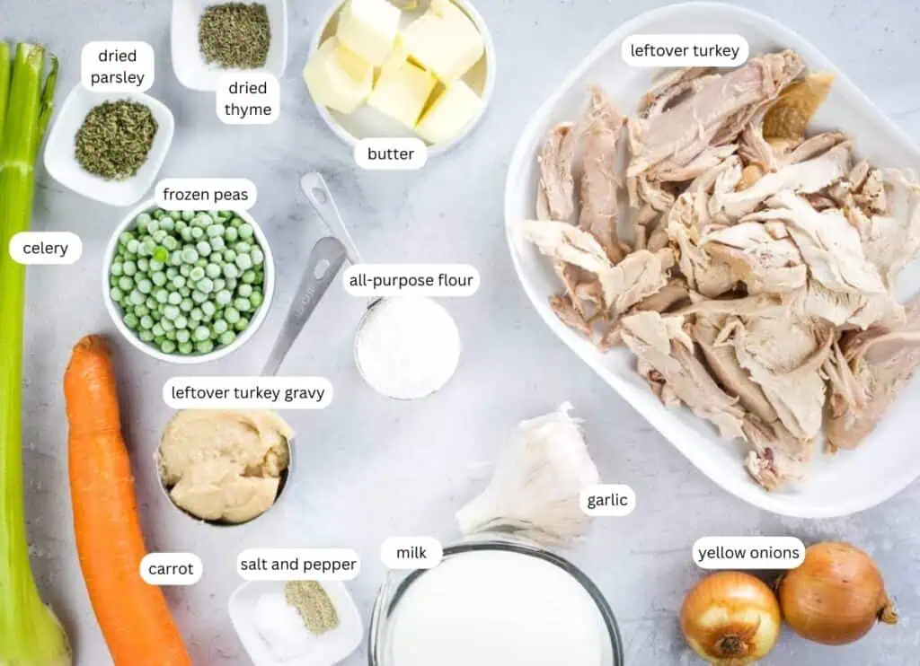 Ingredients for turkey pot pie arranged on a counter, including leftover turkey, vegetables, frozen peas, butter, flour, milk, gravy, and seasonings, each labeled.