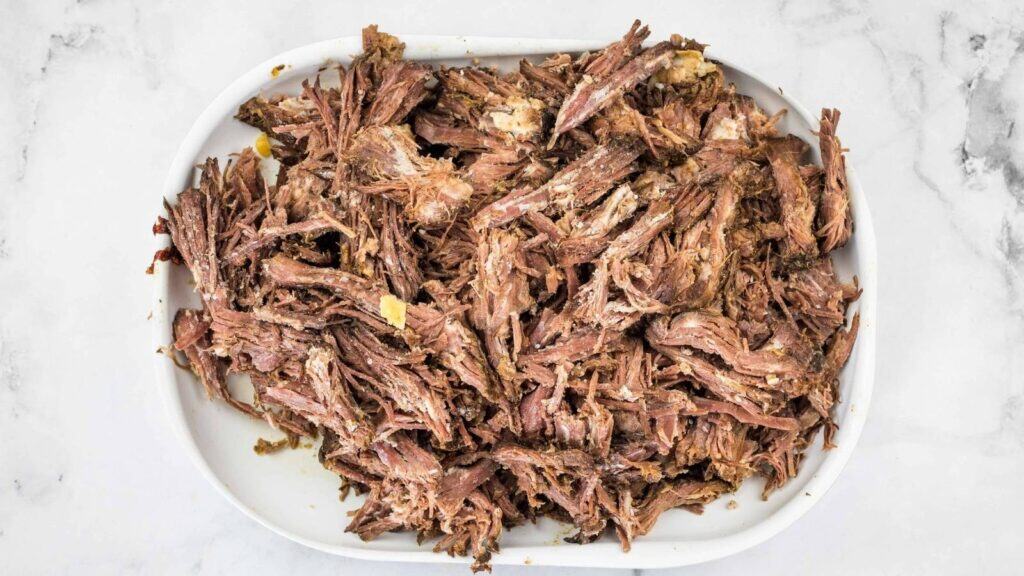 Shredded cooked beef piled on a white plate against a marble background.