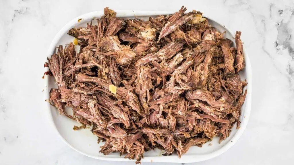 Shredded cooked beef piled on a white plate against a marble background.
