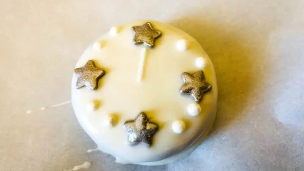 A round white treat decorated with five metallic star-shaped candies and small white candy pearls, arranged in a circular pattern.