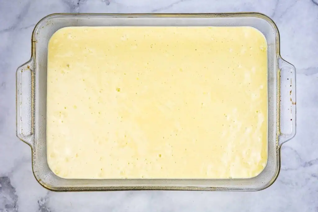 Glass baking dish filled with a smooth, pale yellow liquid mixture on a marble surface, ready to be baked.