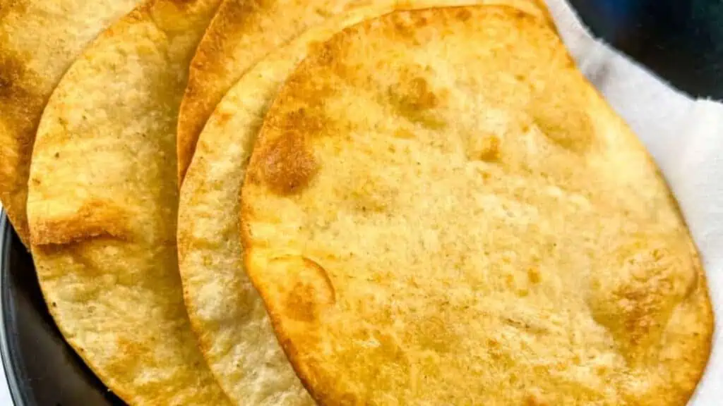 Four crispy, golden-brown tostada shells arranged on a plate with a white napkin.