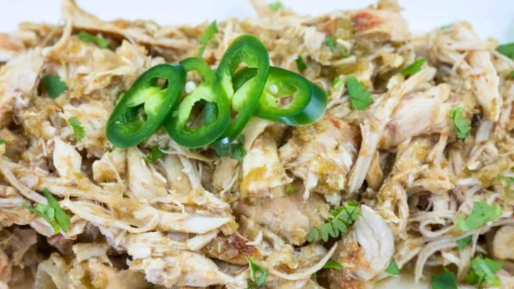 Shredded chicken with green sauce, garnished with sliced jalapeños and fresh cilantro.