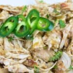 Shredded chicken with green sauce, garnished with sliced jalapeños and fresh cilantro.