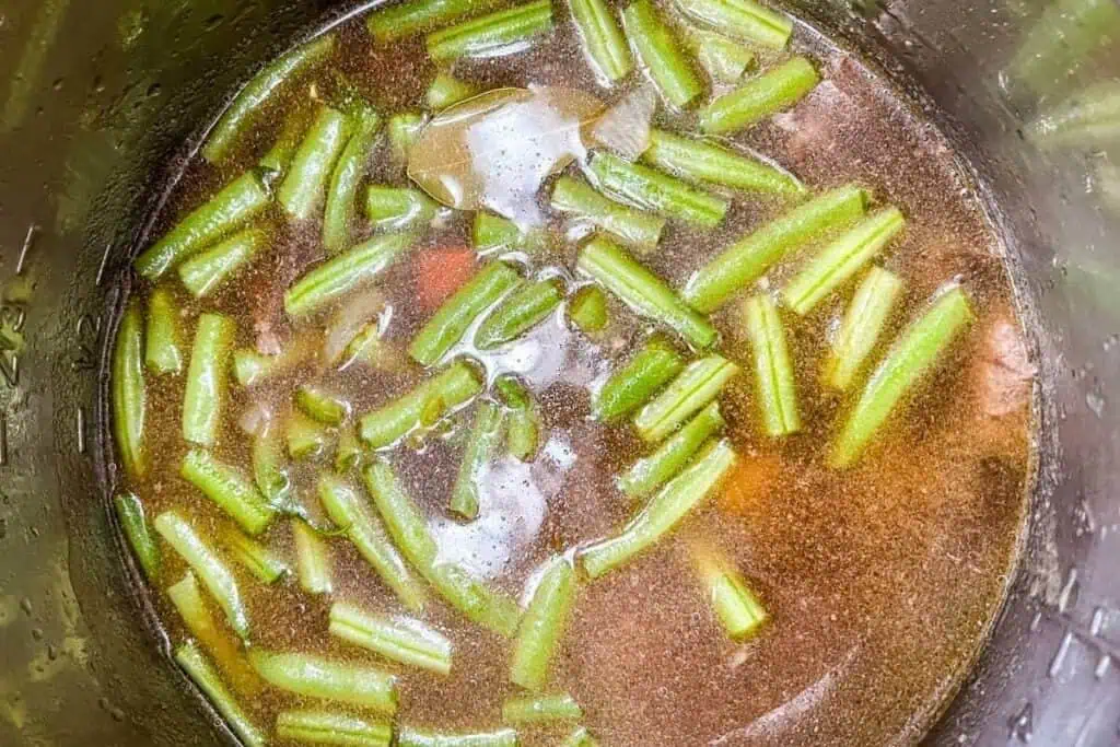 Green beans and chunks of vegetables in a broth, viewed from above inside a pot.
