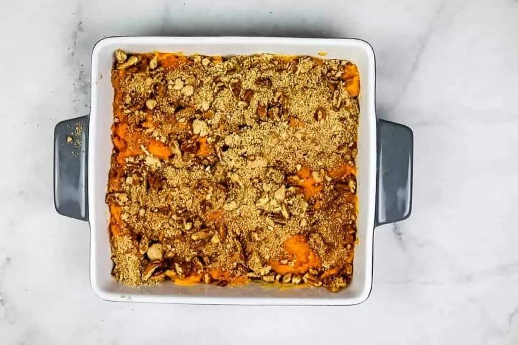 A rectangular baking dish filled with sweet potato casserole topped with a crumbly brown sugar and nut streusel, placed on a light marble surface.