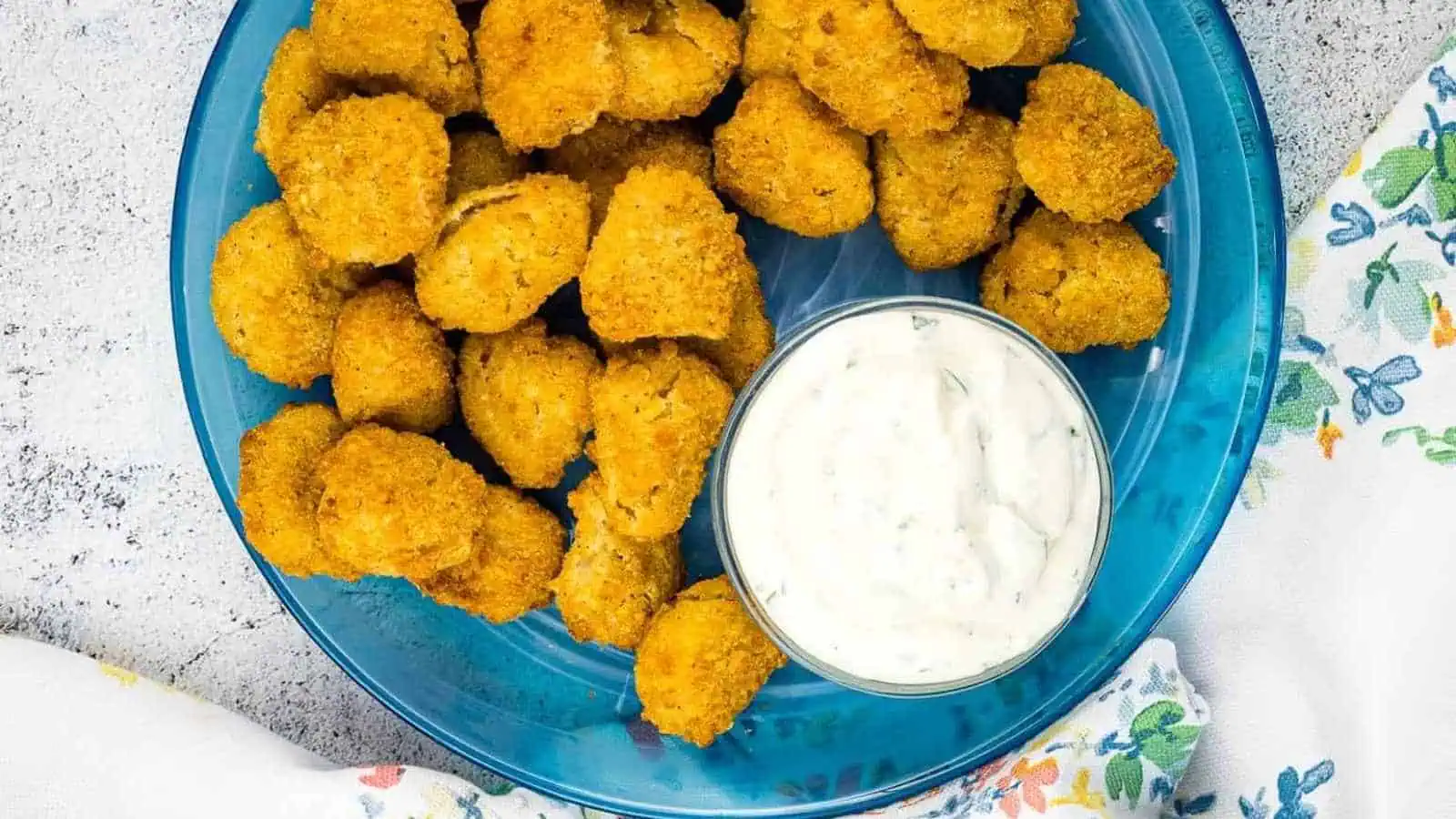 A blue plate with breaded, fried mushroom pieces and a small bowl of white dipping sauce.
