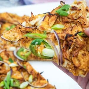A hand holding a slice of BBQ chicken pizza.